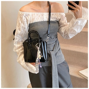 Detail of glossy black patent leather bucket bag with creative billiards charm and top handle