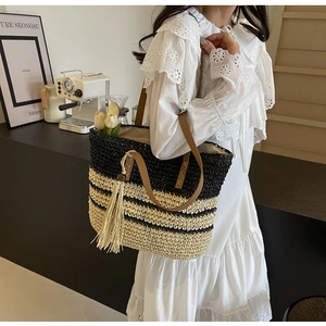 Detail of hand-woven striped tote bag with brown leather handle and beige tassel accent