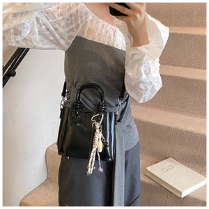 Detail of black glossy leather bucket bag with sphere handle and decorative pendant charm
