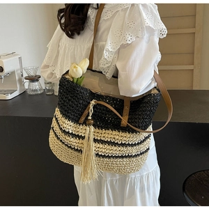 Detail of striped straw tote bag featuring contrast textures and wooden bead tassel