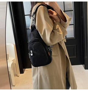 Close-up of black canvas chest bag with multiple zippers and letter print wide strap