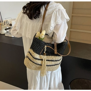 Detail of woven straw tote bag with black stripes and brown leather handle on model