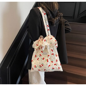 Detail of white tote bag featuring red cherry prints and ruffle edge on a wooden staircase