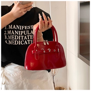Close-up of red glossy shell bag featuring leather strap and silver rivet accents