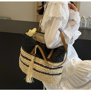 Close-up of woven straw tote bag featuring contrast stripes and leather strap detail