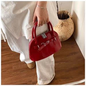 Close-up of red patent leather shell bag featuring silver eyelets and buckle details