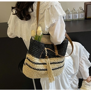 Close-up of woven straw tote bag with black stripes and wood bead tassel detail