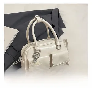 Close-up of cream Boston bag with PU leather texture, front pockets, and pearl heart charm