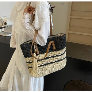 Detail of striped woven tote bag featuring long cream tassels and brown leather handles
