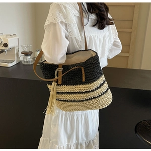 Detail of woven straw tote bag with black stripes, leather straps, and fringe tassel