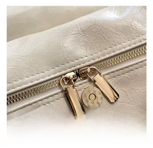 Close-up of polished light gold dual zippers and magnetic snap on creamy leather bag