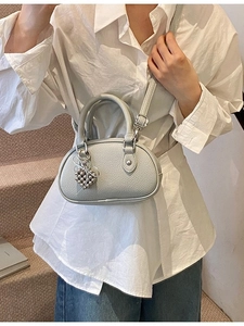 Sac à main ovale gris clair texture litchi avec breloque cœur porté par le mannequin