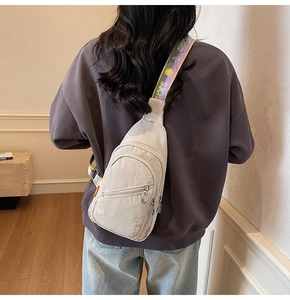 Detail of beige nylon crossbody bag with colorful jacquard strap worn by a model