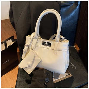 Detail view of cream-white bucket bag with silver metal twist lock and matching mini charm