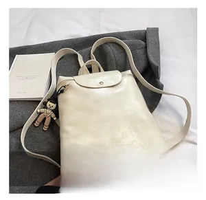 Detail of cream backpack with crinkled texture, flap closure, and a cute doll charm
