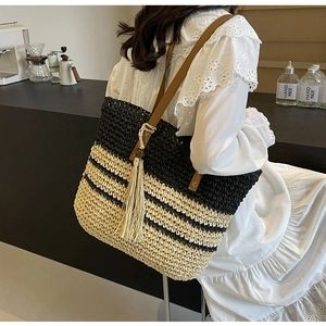 Detail of woven striped tote bag with leather straps and decorative tassel pendant