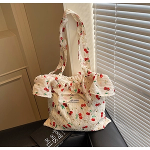 Close-up of white tote bag featuring red cherry print and ruffled edge detail