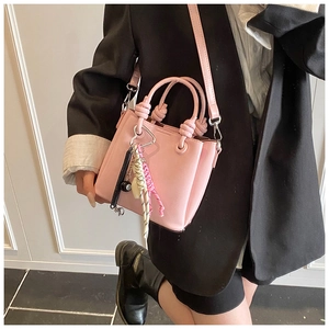Detail of pink mini bucket bag with rope knot handle and decorative charms worn by model