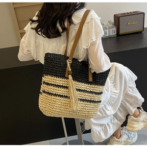 Detail of woven straw tote bag with black stripes and decorative tassels for summer