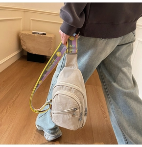 Detail of a beige nylon crossbody bag with multi-layer zippers and a colorful woven strap