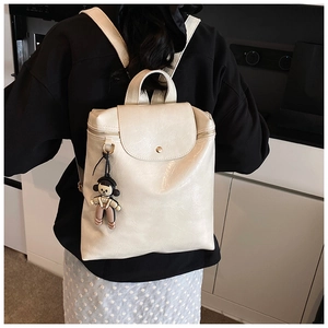 Rear view of model wearing a minimalist cream faux leather backpack with doll pendant