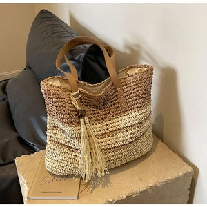Detail of gradient woven straw tote featuring long tassels and premium leather handles