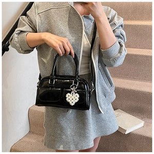 Detail of glossy black patent leather Boston bag with pearl heart charm and front pockets