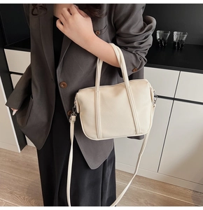 Detail of a minimalist cream-white pebbled leather crossbody bag with silver hardware