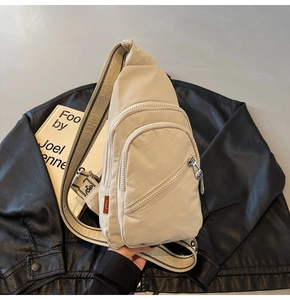 Detail of beige nylon crossbody bag featuring multiple zipper compartments and jacquard strap