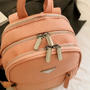 Macro detail of pink lychee leather texture and three polished silver zippers on backpack