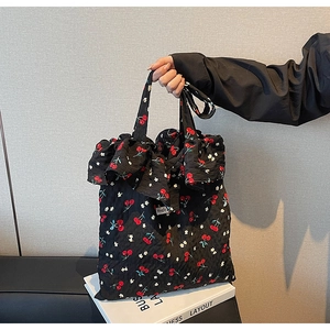Close-up of black floral tote bag featuring red cherry prints and ruffled edges