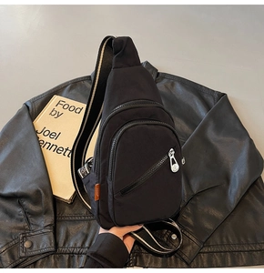 Detail of black nylon chest bag showing three zipper compartments and striped strap