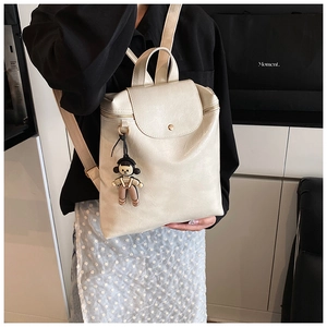 Detail of off-white faux leather backpack with metallic snap and cute cartoon keychain