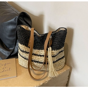 Detailed close-up of woven straw tote bag with black stripes and elegant leather tassel