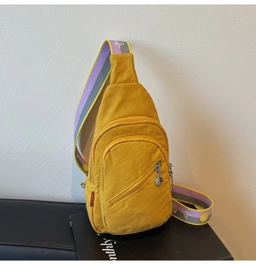 Close-up of a bright yellow nylon sling bag with colorful embroidered woven shoulder strap