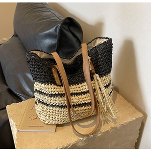 Detail of a large woven tote bag with contrast stripes, leather handles, and side tassels