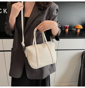 Close-up of cream pebble grain leather handbag with adjustable strap on suit model