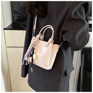 Detail of cream white bucket bag with diverse high-street fashion charms on a model
