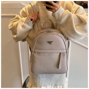 Close-up of beige faux leather backpack featuring vertical quilting and metal triangle logo