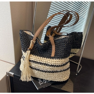 Detail of woven straw tote bag featuring contrast stripes, leather handles and tassel charm