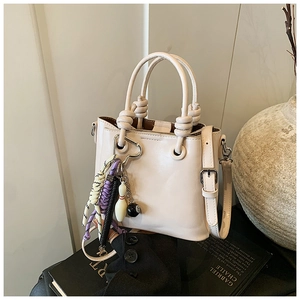 Detail of minimalist cream bucket bag with knot handle and trendy decorative charms