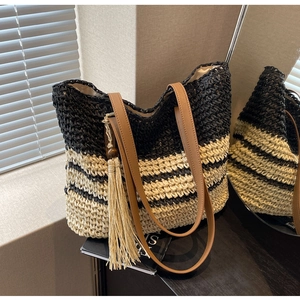 Detail of striped straw tote bag with brown leather straps and tassel charm in a mirror view