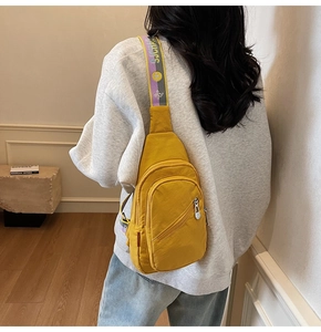 Detail shot of a bright yellow nylon chest bag with a colorful jacquard strap worn by a model