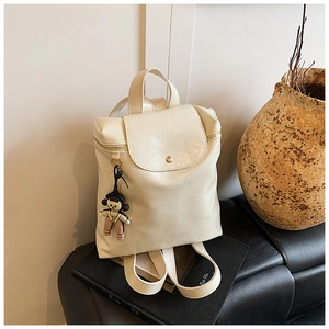Detail of a creamy white mini backpack with pleated texture and cute doll pendant on books