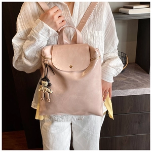 Pink synthetic leather backpack showing wrinkled texture detail and cartoon girl pendant