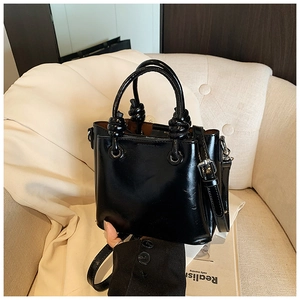 Detail of a black patent leather bucket bag with unique knot handles and silver hardware