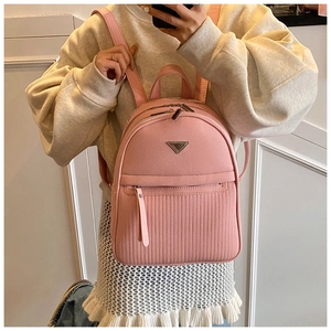 Detail view of pink quilted leather backpack featuring triangle metal logo and zip closure