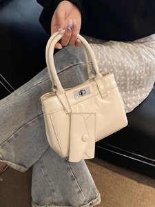 Minimalist beige leather bucket bag with silver twist lock shown in a casual setting