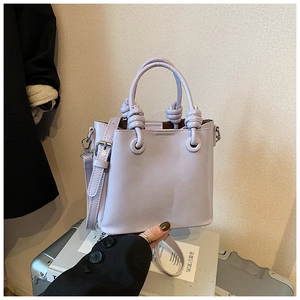 Detail of light purple bucket bag featuring a decorative knotted handle and matte finish