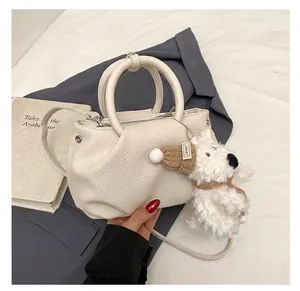 Detail showing beige pebbled leather bucket bag with cute dog charm and metallic eyelets